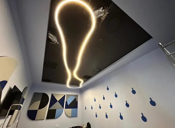 Corp de iluminat LED în formă de bec, montat pe un tavan negru, într-o cameră cu tablouri decorative pe perete