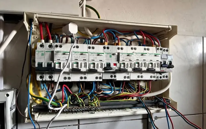 Tablou electric vechi, cu cabluri încurcate care ies din aparatele de protecție